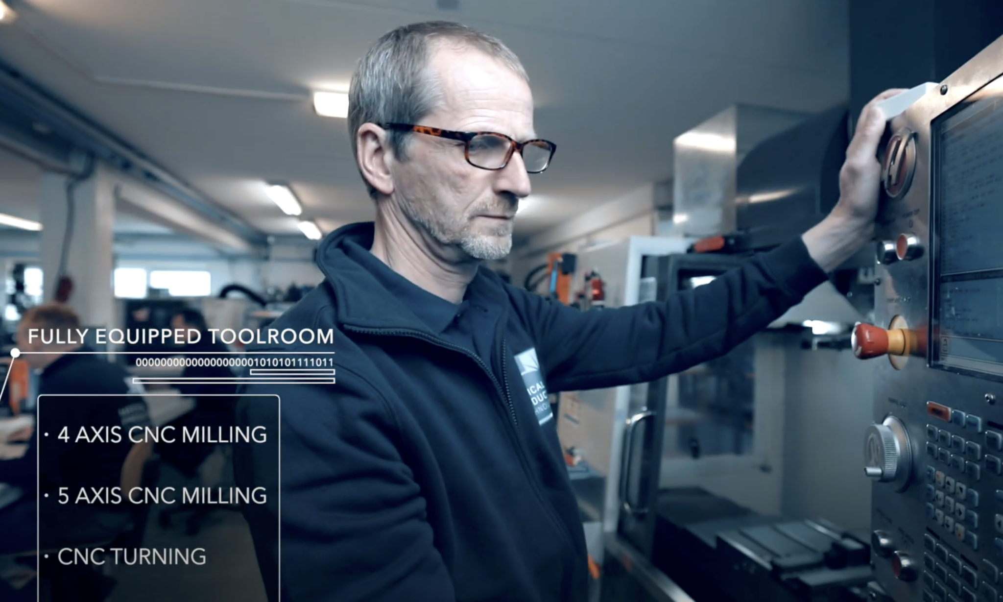 Industriële foto van een werknemer met bril die bij het bedieningspaneel van een CNC-freesmachine aan het werk is.