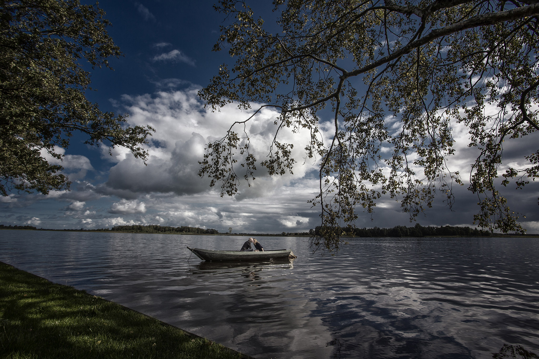 Een meer met een prachtige wolkenlucht. Op het meer drijft ene metalen bootje met een verliefd koppel aan boord