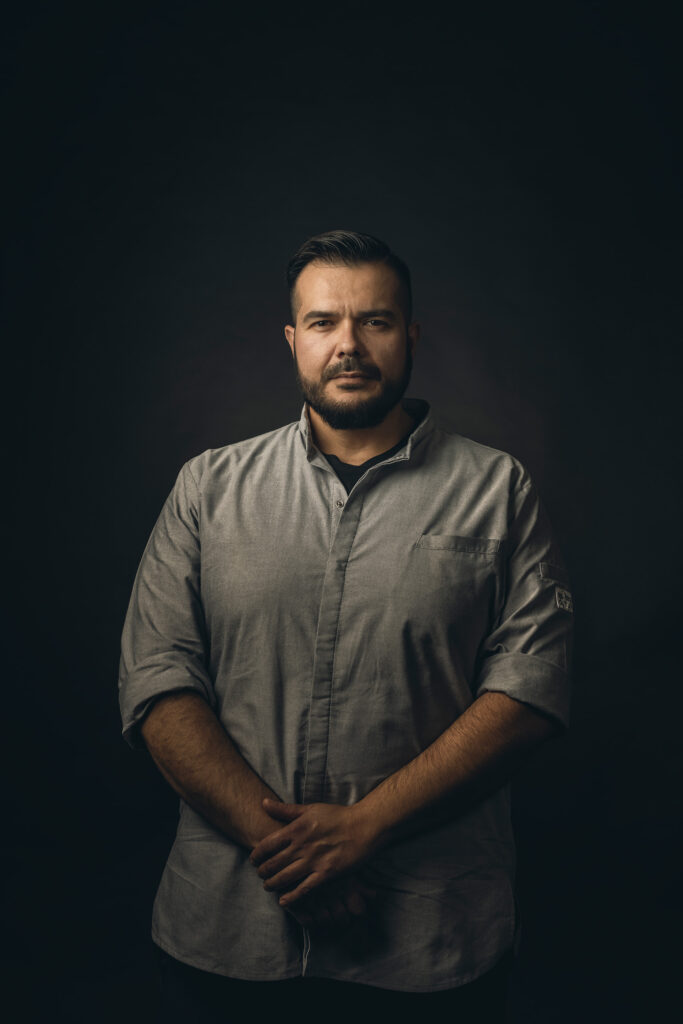 Chefkok van Griekse afkomst poseert statig voor een donkere achtergrond