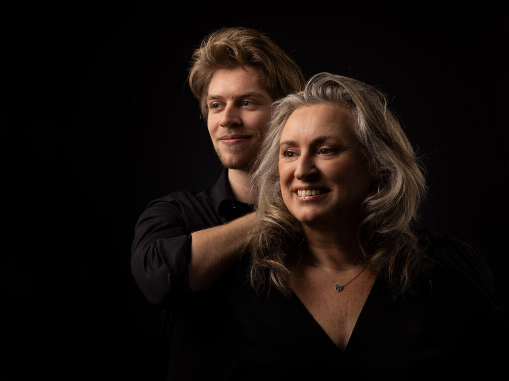 Moeder kijkt lachend langs de camera met haar zoon achter haar.