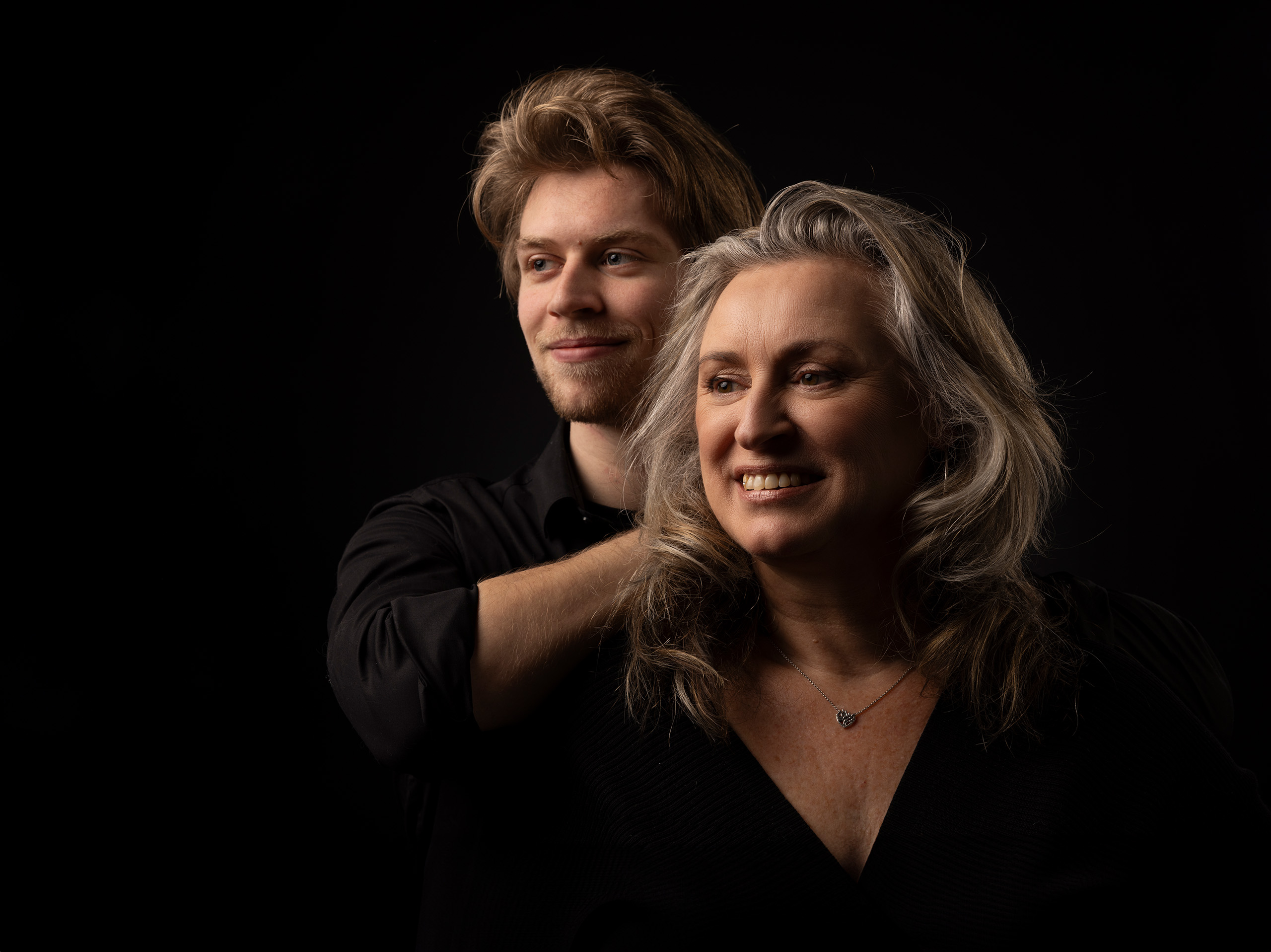 Moeder kijkt lachend langs de camera met haar zoon achter haar.