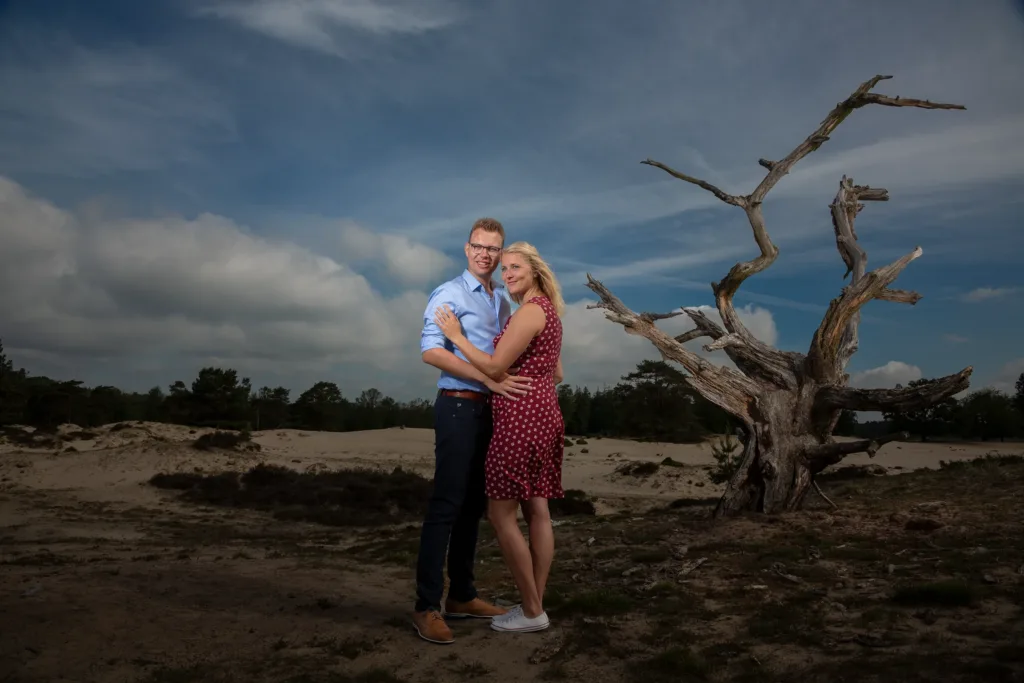 Jonge vrouw omarmd door haar verloofde op een zandvlakte onder een dramatische wolken lucht